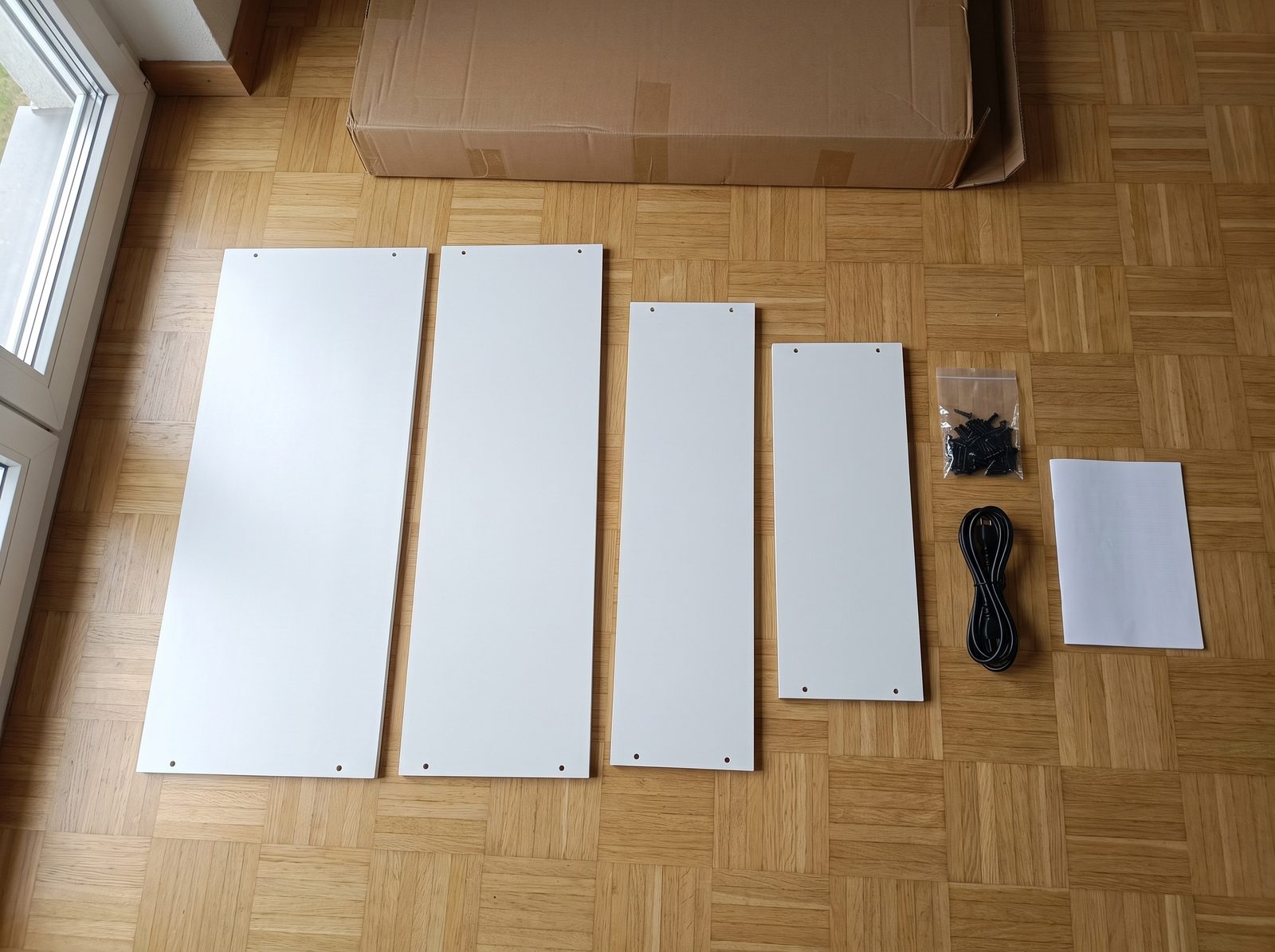 Les panneaux de PVC blanc etales au sol a cote du carton ouvert, avec la visserie et la notice